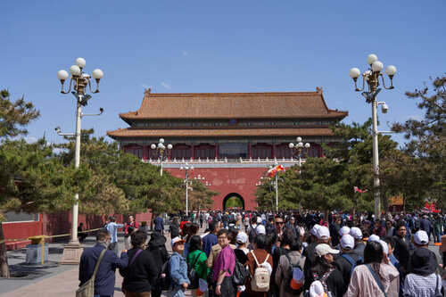 Touristen vor dem Meridian-Tor der Verbotenen Stadt Peking Menschenmenge vor dem südlichen Eingang der Verbotenen Stadt in Peking, dem Meridian-Tor; traditionelle chinesische Architektur mit roter Fassade und verzierten Dachziegeln, flankiert von Bäumen und Straßenlaternen bei klarem Himmel